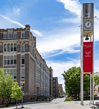 A photo of the New Jersey Institute of Technology (NJIT) on a sunny day. On the left are brick buildings, while on the right is a clock tower with the NJIT logo on it.